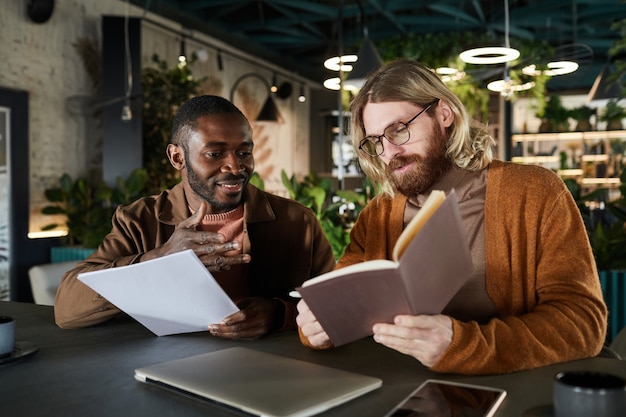 Portrait of two contemporary men collaborating on project during business meeting in green office or cafe interior, copy space