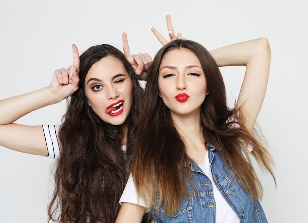 Portrait of two cute playful women showing horns with fingers on head