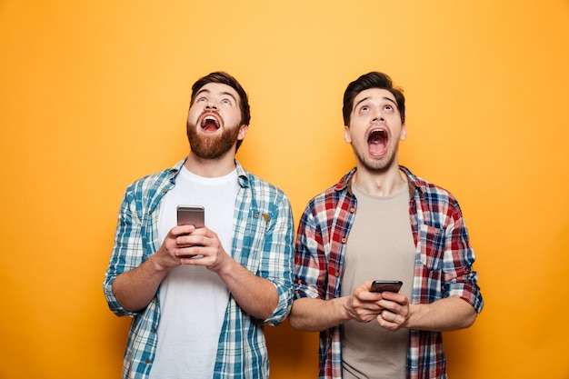 Portrait of a two excited young men holding mobile phones