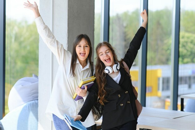 Portrait of two female college students with books smiling and standing at high school hall