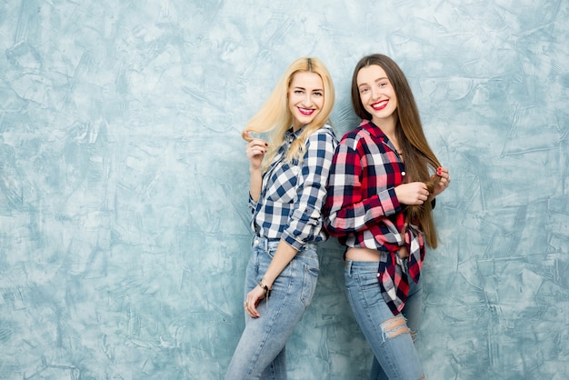 Portrait of two female friends in checkered shirts and jeans together on the blue painted wall background