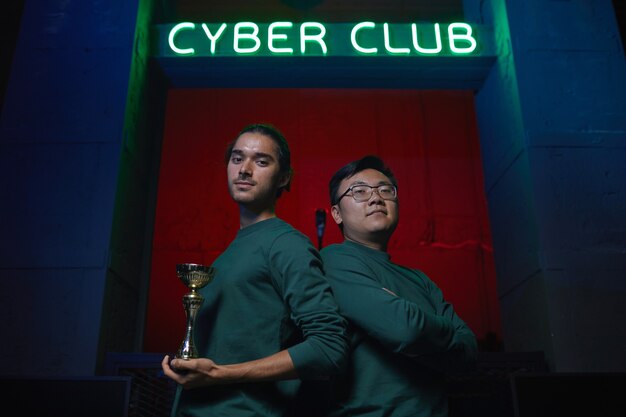 Portrait of two gamers standing back to back looking at camera and holding cup After competition in computer game