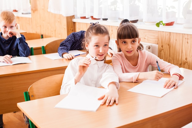 Portrait of two girlfriends who sitting at the same desk in the classroom