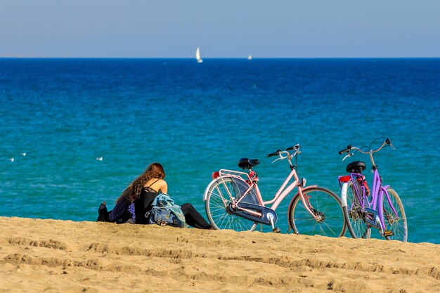 Foto ritratto di due ragazze coppia seduta sulla sabbia in riva al mare con le biciclette.