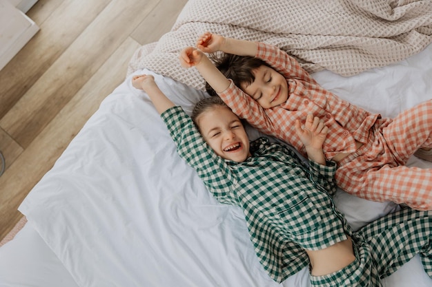 ベッドに横たわっている2人の女の子の肖像画そして素晴らしい睡眠の後ちょうど目覚め伸びた後写真のためにポーズをとっています