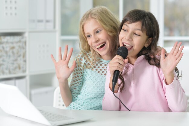 Portrait of two girls using laptop and microphone at home