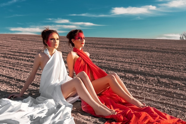 Portrait of two girls with creative body art and makeup sitting on the bare ground