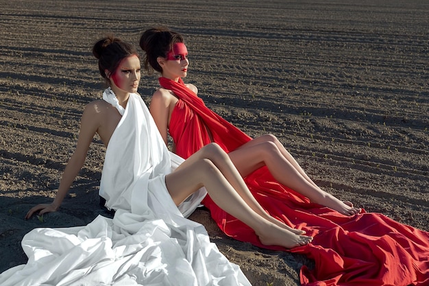 Portrait of two girls with creative body art makeup sitting on the bare ground