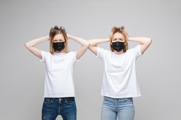 Портрет двух красивых девушек с длинными светлыми волосами с черными медицинскими масками на их лицах паники изолированы