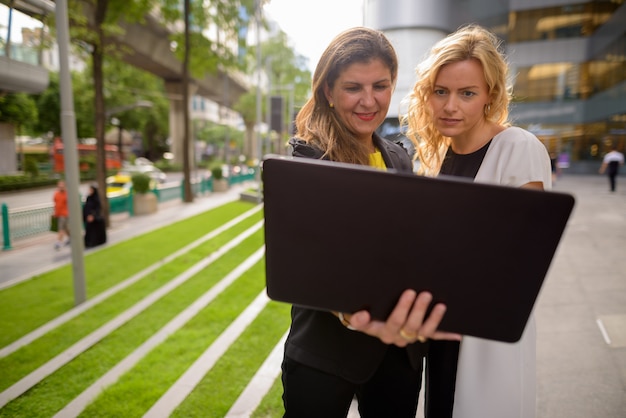 Portrait of two happy businesswoman using laptop computer together outdoors