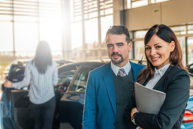 車のショールームの中で働いている2人の幸せな車販売コンサルタントの肖像画。