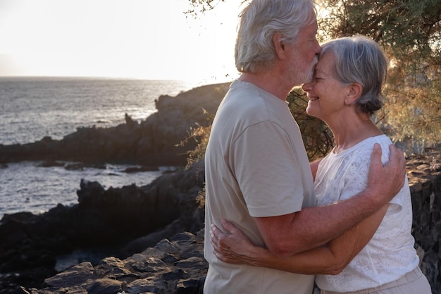 Ritratto di due anziani o pensionati felici e romantici abbracciati al mare alla luce del tramonto anziani all'aperto che si godono le vacanze insieme