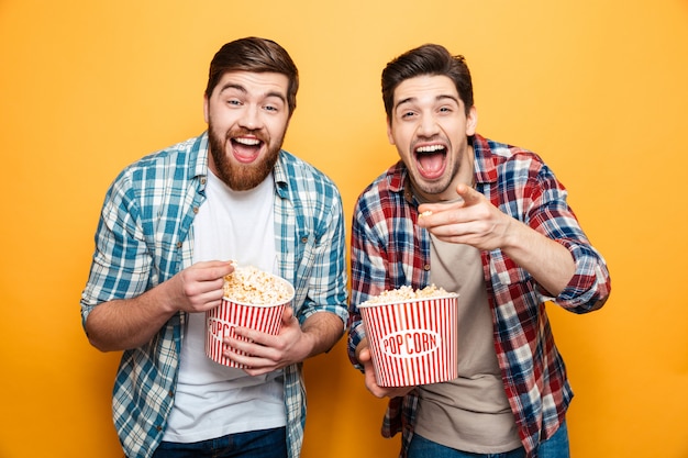 Портрет двух счастливых молодых людей едят попкорн