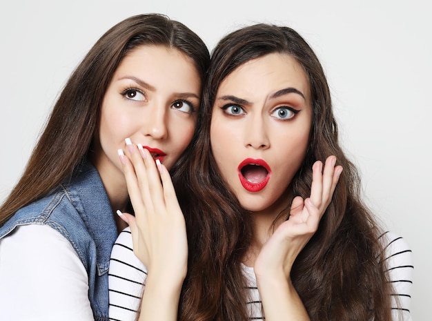 Portrait of two happy young women sharing secrets isolated over white background