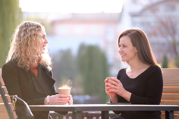 Portrait of two happy young women sitting at city street
cafe