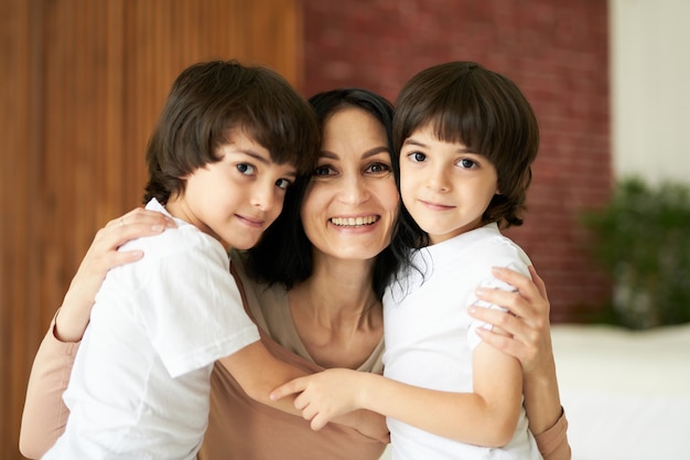 Portrait of two latin children little twin boys smiling at camera and hugging their mom