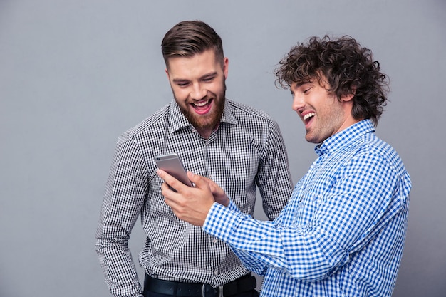 Portrait of a two laughing men using smartphone over gray wall