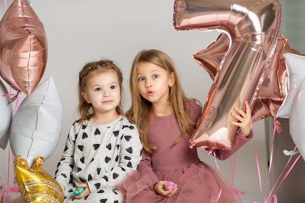 Portrait of two little cute girls sitting on the floor with balloons