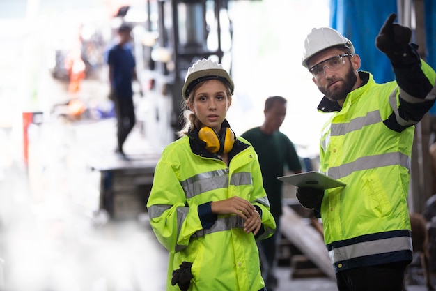 portrait of two manufacturing staff or engineers discussing and operating machine in factory.