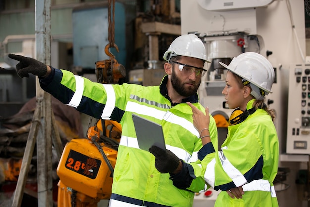 portrait of two manufacturing staff or engineers discussing and operating machine in factory.