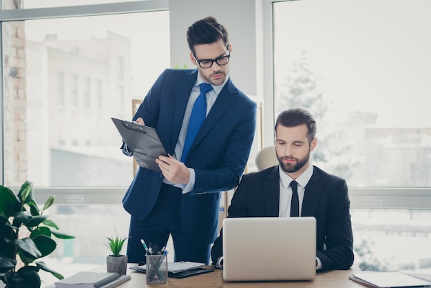 Portrait of two nice attractive handsome smart clever skilled qualified men banker economist financier developing it startup researching market data in light white interior work place station