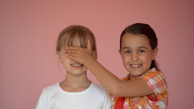 Portrait of two nice-looking attractive charming cute lovely\
friendly cheerful pre-teen girls isolated on pink pastel\
background