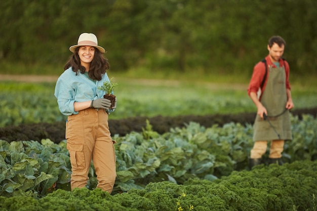 Photo portrait of two people working in field at vegetable plantation, focus on young woman smiling at camera in foreground, copy space