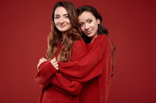 Portrait of two pretty crazy sisters best friends twins in fashion cozy winter sweater posing