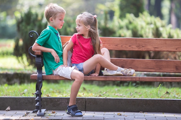 Photo portrait of two pretty cute children boy and girl having fun time on a bench in summer park outdoors.