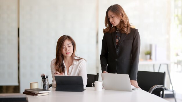 Portrait of two professional businesswomen discussing on their current project together in modern office