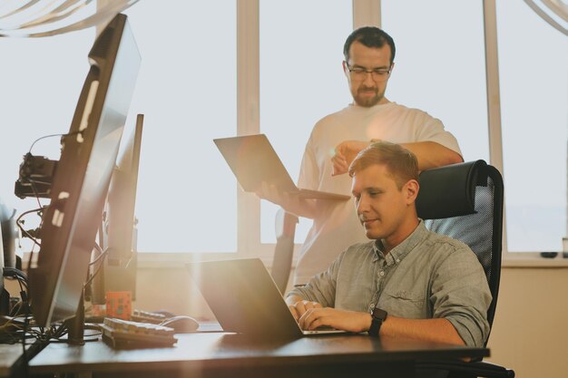 Portrait of two professional male programmers working on computer in diverse offices Modern IT technologies development of artificial intelligence programs applications and video games concept