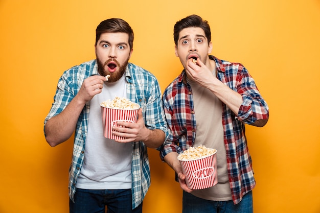 Portrait of a two scared young men eating popcorn