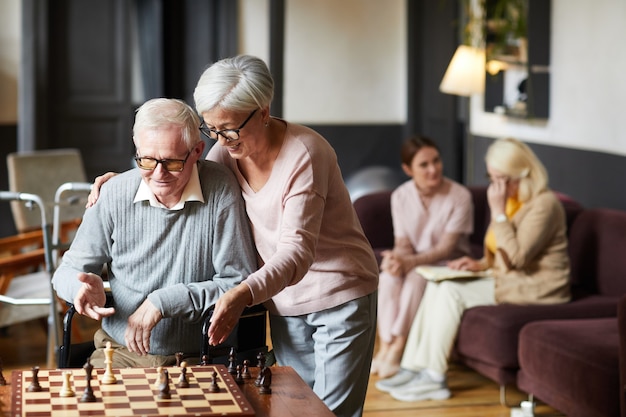 Portrait of two senior people playing chess and enjoying activities in retirement home copy space