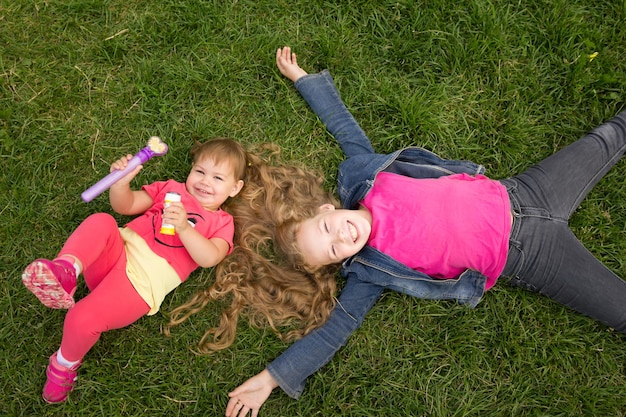 A portrait of two sisters on green grass park outdoor  top view