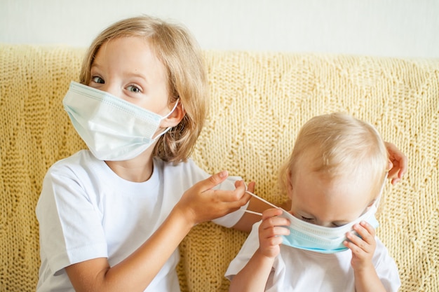 Photo portrait of two sisters putting on medical protective masks the older sister helps the younger