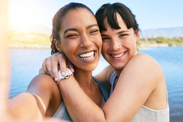 Portrait of two smiling friends taking selfies together for social media on a lake over summer break Smiling happy women bonding and hugging outside in nature Embracing and having fun on weekend