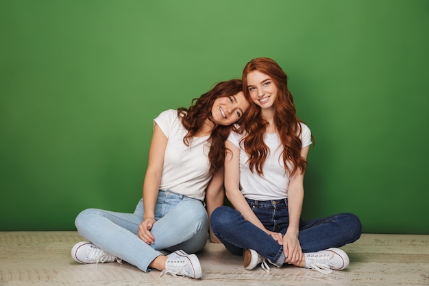 Портрет двух улыбающихся молодых рыжих девушек, сидящих на полу