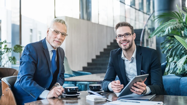 Portrait of two successful businessmen working and sitting on sofa in office lobby