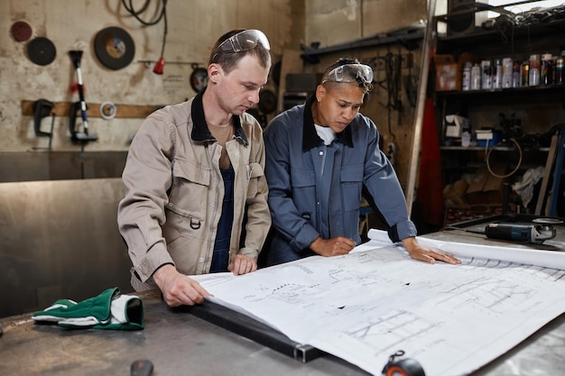 Portrait of two workers looking at blueprints and plans in industrial factory workshop