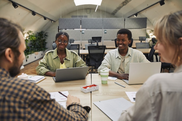 Ritratto di due giovani afro-americani sorridenti a partner commerciali seduti sul tavolo durante la riunione in un ufficio moderno, copia dello spazio