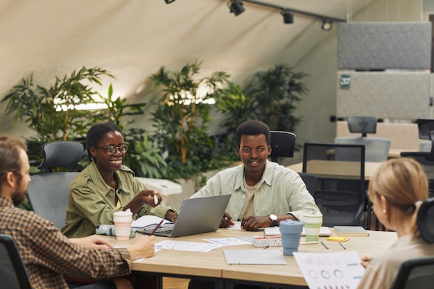 현대 사무실에서 회의 및 작업 프로젝트를 논의하는 동안 테이블에 앉아있는 동안 동료에 웃고 두 젊은 아프리카 계 미국인 사람들의 초상화, 복사 공간
