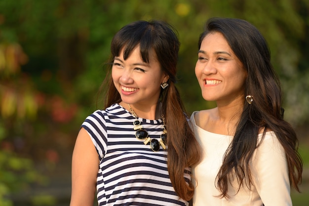 Portrait of two young Asian women together relaxing at the park outdoors