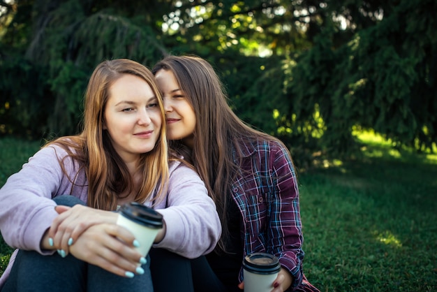 Portrait of two young beautiful girls sitting next to each other on the green lawn in the Park,