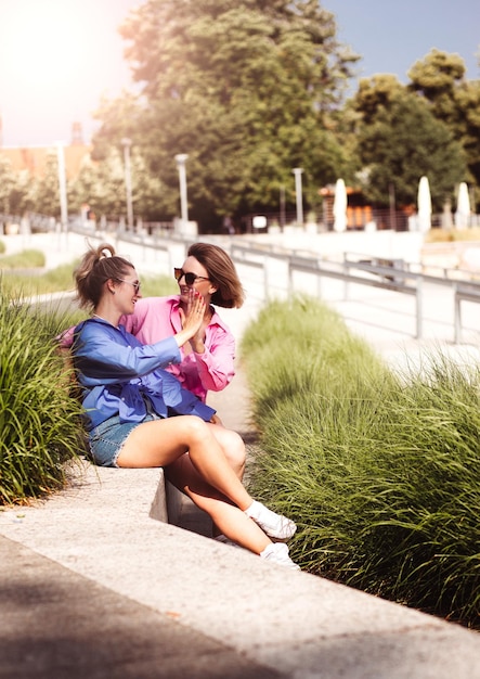 Portrait of two young beautiful smiling hipster female in trendy summer color clothes carefree women posing on river background Positive models having fun hugging