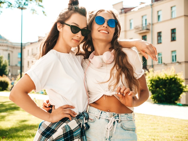 Portrait of two young beautiful smiling hipster girls in trendy summer white t-shirt clothes