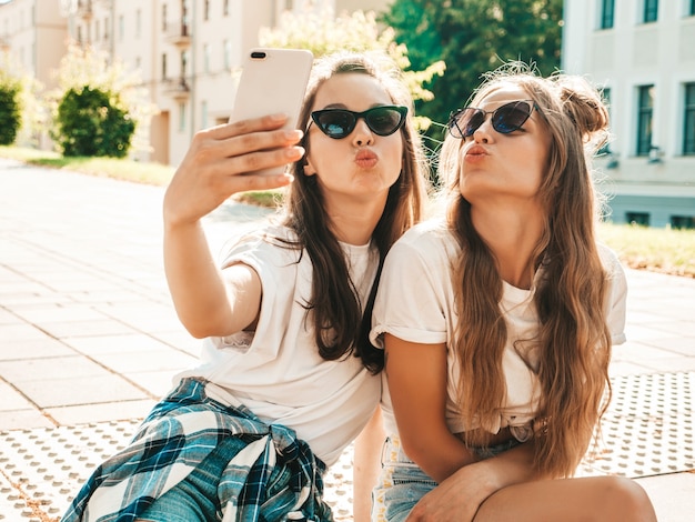 Ritratto di due giovani belle donne hipster sorridenti in vestiti di t-shirt bianca estiva alla moda