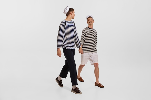 Portrait of two young boys sailor seamen in striped shirts walking on deck isolated over white