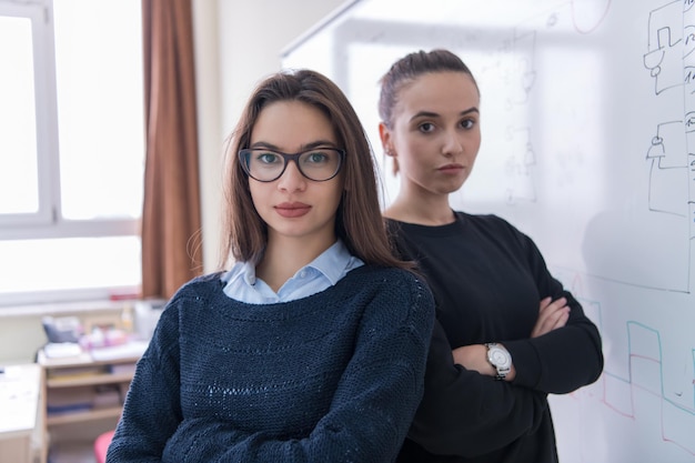 白い黒板の前に立ってカメラを見ている2人の若い女子学生の肖像画