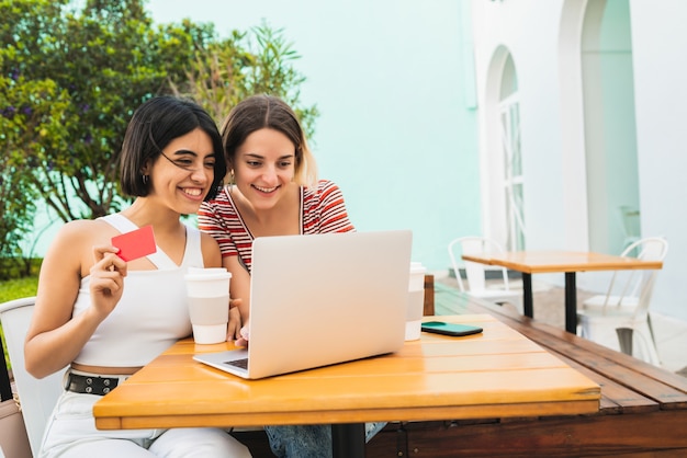 Portrait of two young friends doing online shopping with laptop and credit card at coffee shop.