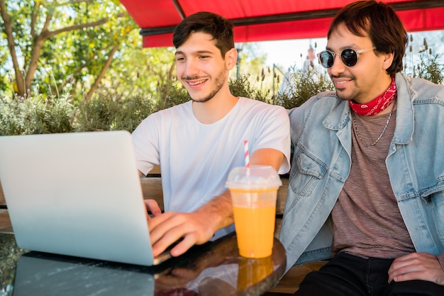 Portrait of two young friends using a laptop while sitting outdoors at coffee shop